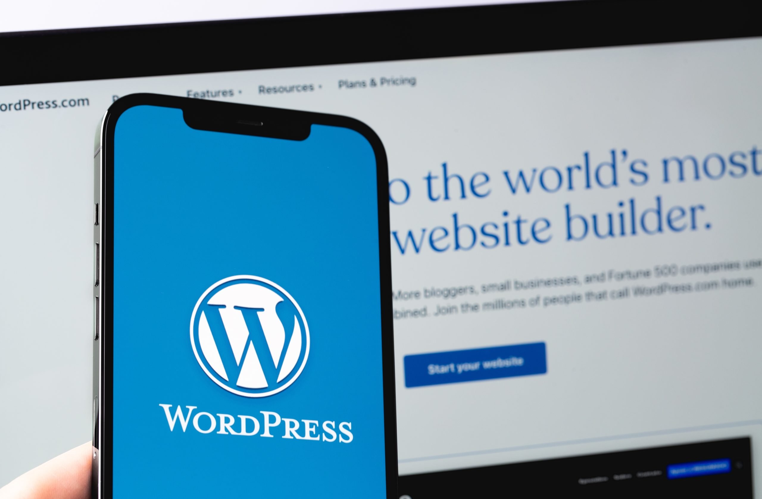A person holding a mobile with WordPress logo infront of a laptop with WordPress site on screen
