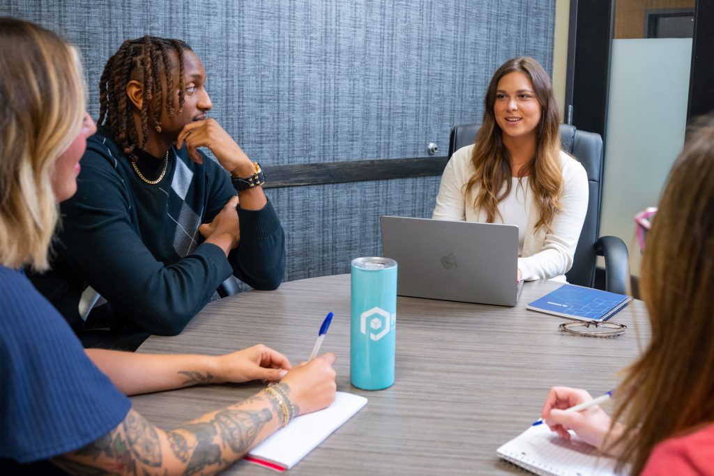 3 women and 1 man seated around a table with notepads and a computer