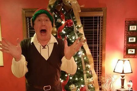 man dressed as an elf standing in front of Christmas tree