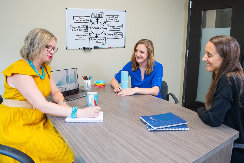 3 team members in a group, one making notes on paper
