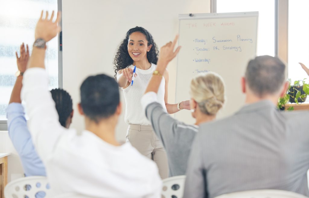 A group of people in a learning setting with their hands raised.
